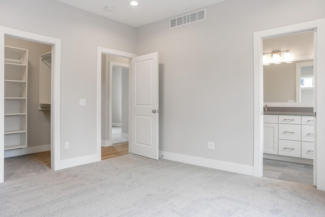 unfurnished bedroom with baseboards, a walk in closet, visible vents, and light colored carpet