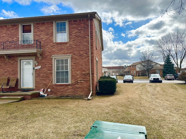 view of side of home with brick siding, a yard, and a balcony