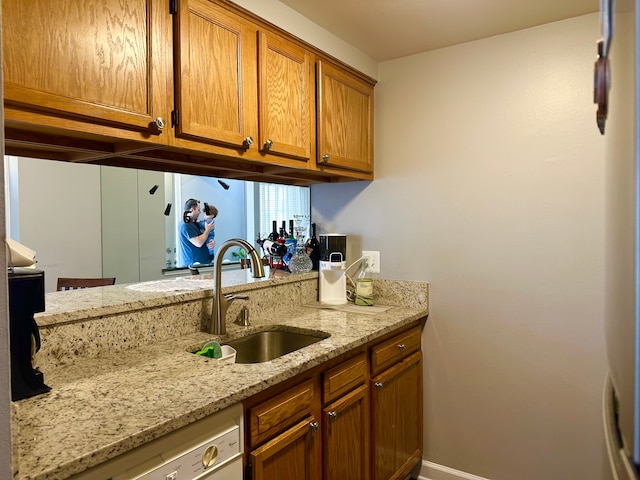 kitchen featuring dishwashing machine, light stone counters, a sink, baseboards, and brown cabinets