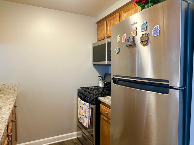 kitchen with baseboards, stainless steel appliances, light stone countertops, and brown cabinets