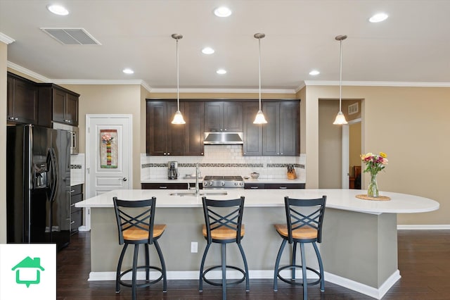 kitchen with a sink, under cabinet range hood, dark brown cabinetry, black fridge, and dark wood-style flooring