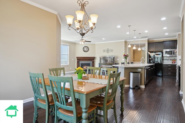 dining area with dark wood-type flooring, a warm lit fireplace, a ceiling fan, and crown molding