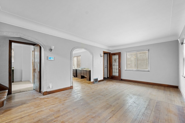 unfurnished living room with visible vents, baseboards, arched walkways, ornamental molding, and hardwood / wood-style flooring