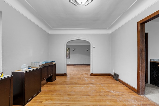 hall with light wood-style floors, arched walkways, and baseboards