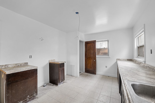 kitchen with dark brown cabinets, light countertops, baseboards, and a sink