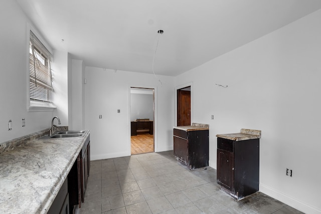 kitchen featuring dark brown cabinets, light countertops, baseboards, and a sink