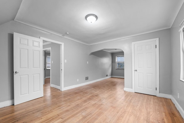 empty room with arched walkways, visible vents, baseboards, and light wood-style floors