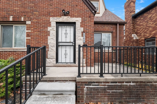 entrance to property featuring brick siding and roof with shingles