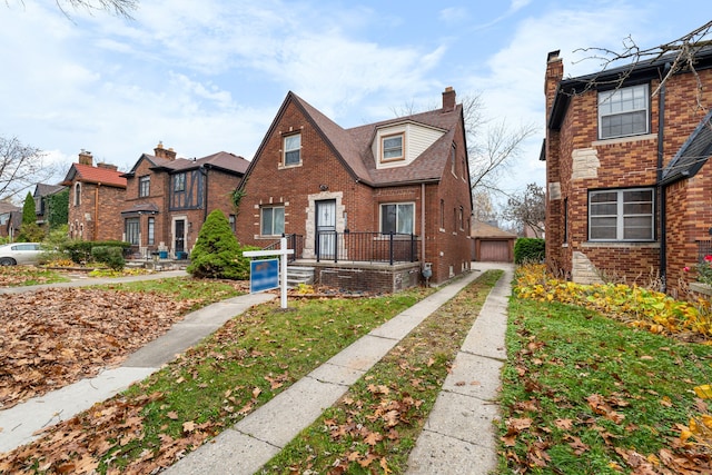 view of front of house featuring brick siding, a chimney, and an outdoor structure