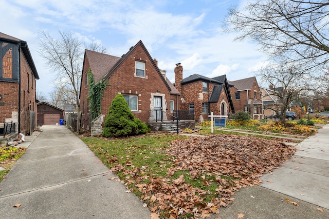 tudor-style house featuring an outdoor structure, a garage, brick siding, and a residential view