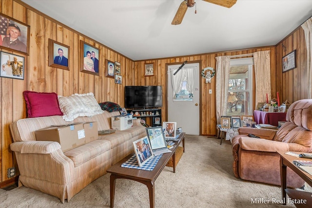 living area with wood walls, ceiling fan, and light colored carpet