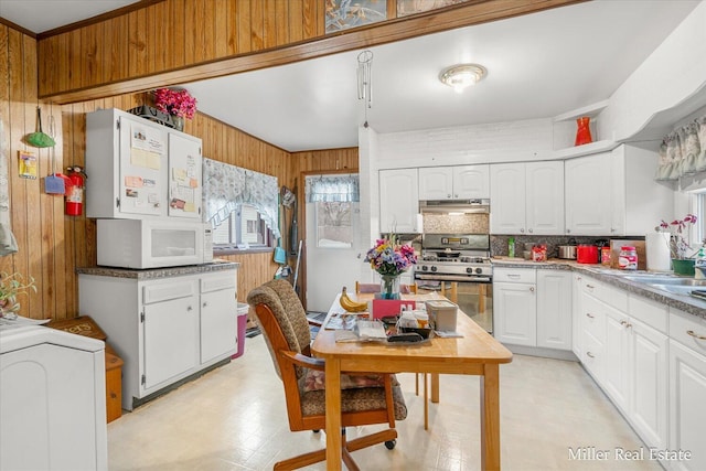 kitchen with wooden walls, under cabinet range hood, white cabinetry, stainless steel gas range, and light floors