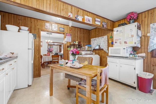 kitchen with white appliances, wooden walls, washer / clothes dryer, light floors, and white cabinetry