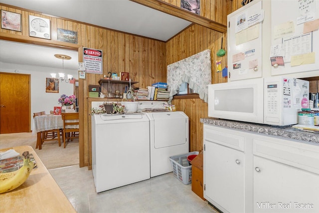 clothes washing area featuring an inviting chandelier, wooden walls, and washer and clothes dryer