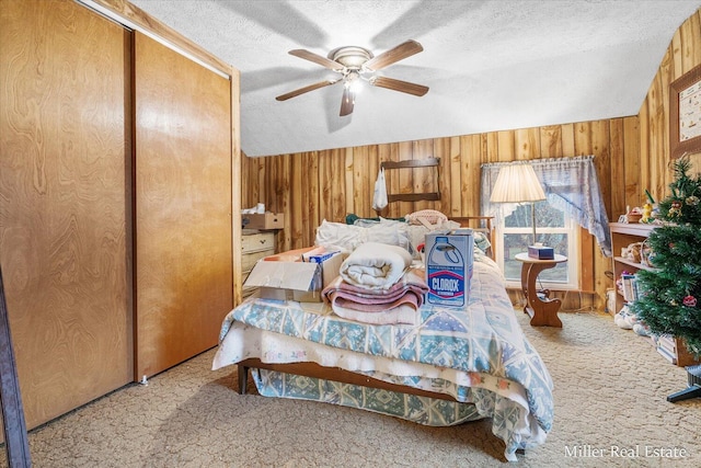 carpeted bedroom featuring a textured ceiling, ceiling fan, wood walls, and vaulted ceiling