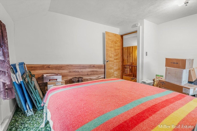 bedroom with a wainscoted wall, wooden walls, vaulted ceiling, and a textured ceiling