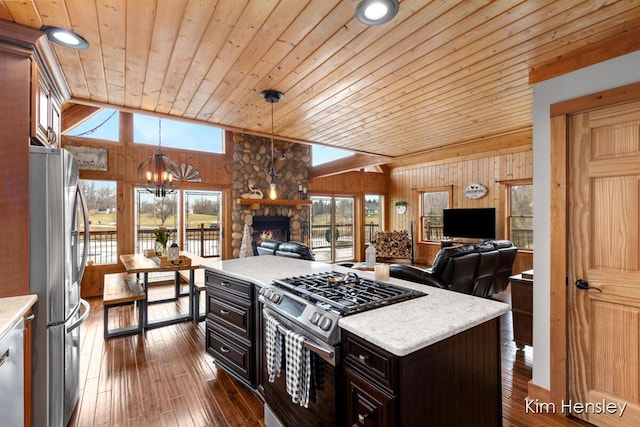 kitchen with lofted ceiling, wooden walls, open floor plan, appliances with stainless steel finishes, and dark wood finished floors