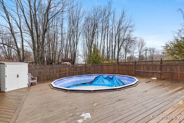 view of pool featuring a fenced in pool, a fenced backyard, an outbuilding, a deck, and a shed