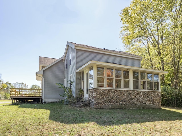 view of home's exterior featuring stone siding, a lawn, a wooden deck, and a sunroom