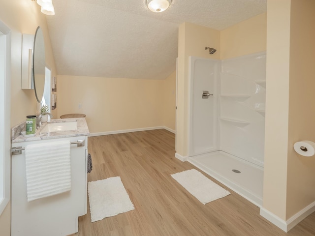 bathroom with baseboards, a shower, wood finished floors, vaulted ceiling, and a textured ceiling