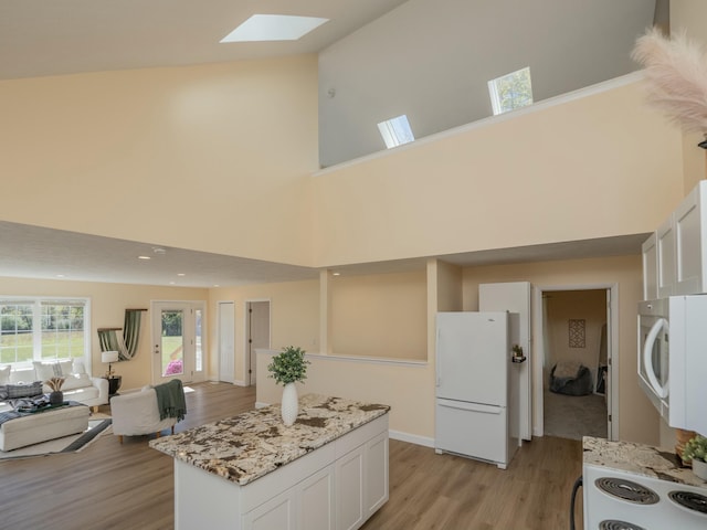 kitchen featuring white appliances, a skylight, white cabinets, open floor plan, and light wood-type flooring