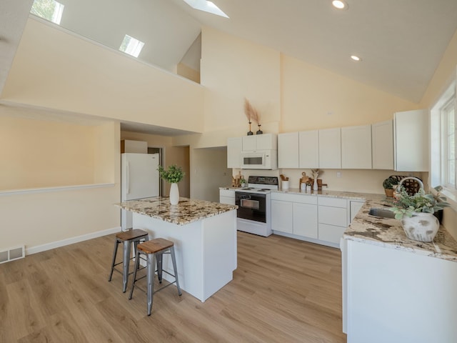 kitchen featuring white appliances, a skylight, visible vents, a kitchen island, and a sink