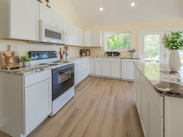 kitchen with light wood finished floors, white cabinets, vaulted ceiling, a sink, and white appliances