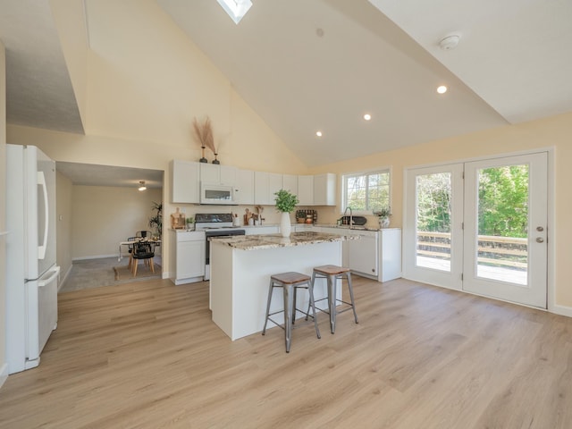 kitchen with light wood-style flooring, white appliances, a breakfast bar, a kitchen island, and white cabinets