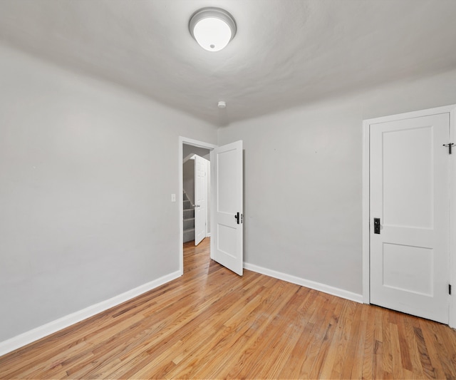 unfurnished room featuring light wood-type flooring, baseboards, and stairs