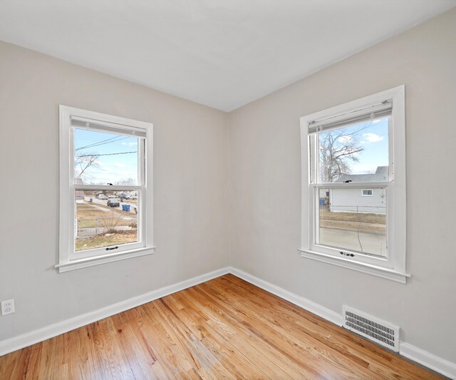 empty room featuring hardwood / wood-style flooring, visible vents, and baseboards