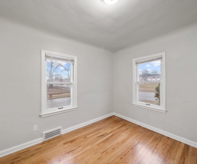 spare room featuring a wealth of natural light, hardwood / wood-style flooring, visible vents, and baseboards