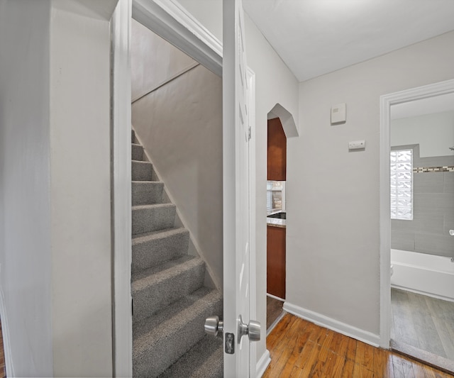 staircase with arched walkways, wood-type flooring, and baseboards