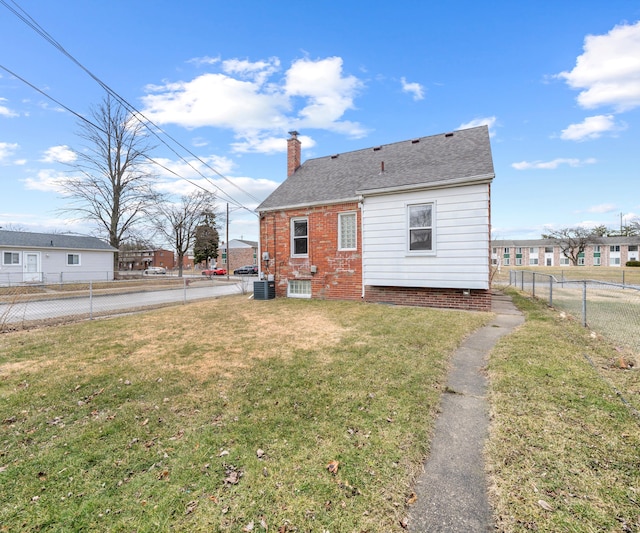 rear view of property with brick siding, a yard, a chimney, central AC, and fence