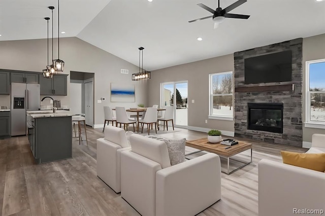living room featuring high vaulted ceiling, a large fireplace, ceiling fan with notable chandelier, and light wood-type flooring