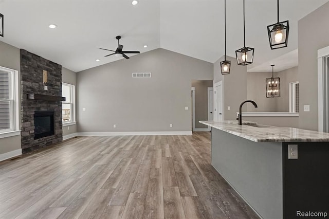 kitchen with visible vents, light wood-style flooring, a sink, a stone fireplace, and ceiling fan with notable chandelier