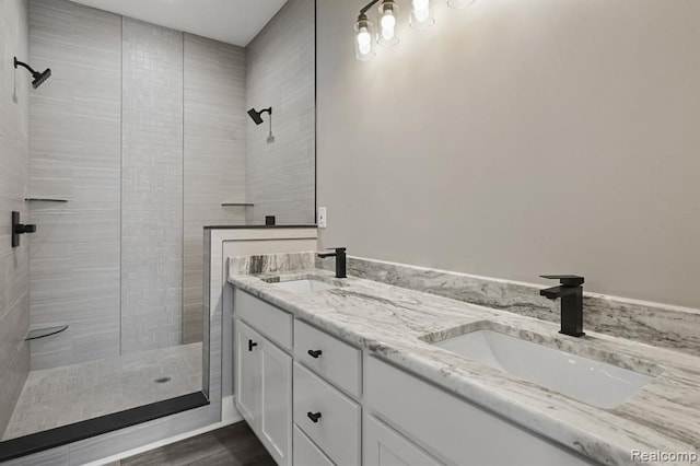 full bath featuring double vanity, tiled shower, and a sink