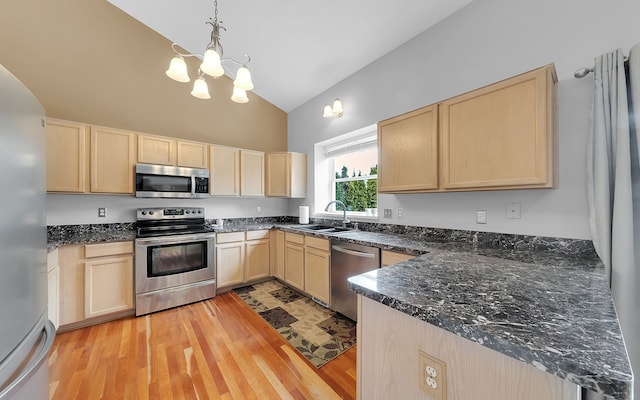 kitchen featuring light brown cabinets, vaulted ceiling, appliances with stainless steel finishes, light wood-style floors, and a sink