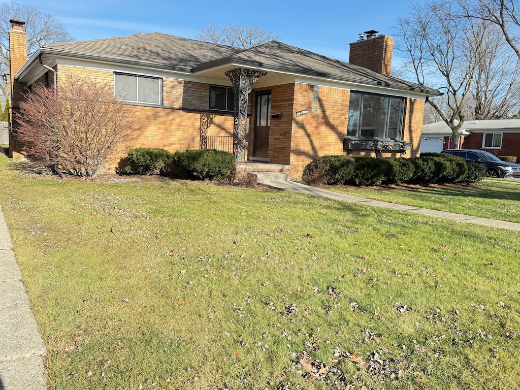 view of front of home with brick siding, a chimney, and a front yard