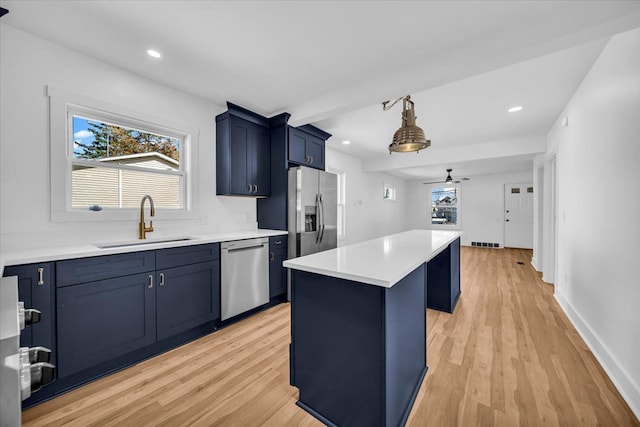 kitchen featuring blue cabinetry, a kitchen island, light wood-type flooring, appliances with stainless steel finishes, and a sink