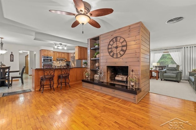 living room with light wood finished floors, visible vents, a ceiling fan, and a multi sided fireplace