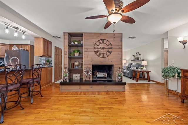 living room featuring light wood-type flooring, a large fireplace, baseboards, and a ceiling fan