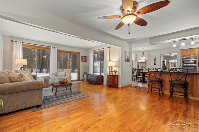 living area featuring ceiling fan, plenty of natural light, baseboards, and light wood-style floors