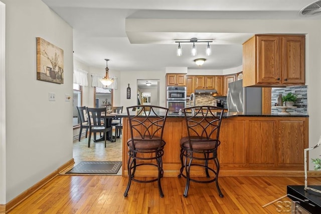 kitchen with stainless steel appliances, a peninsula, visible vents, decorative backsplash, and brown cabinetry