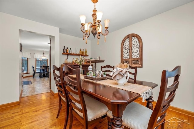 dining area with baseboards, a notable chandelier, and light wood finished floors