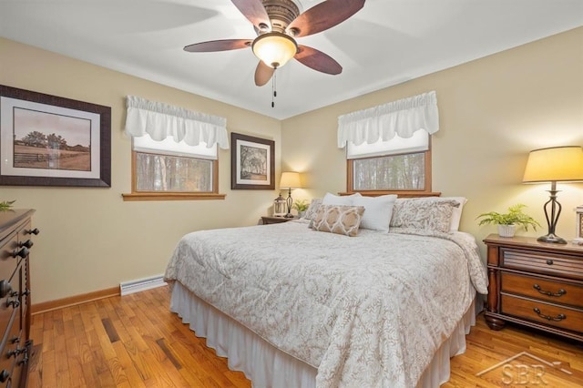 bedroom featuring a baseboard heating unit, light wood-type flooring, ceiling fan, and baseboards