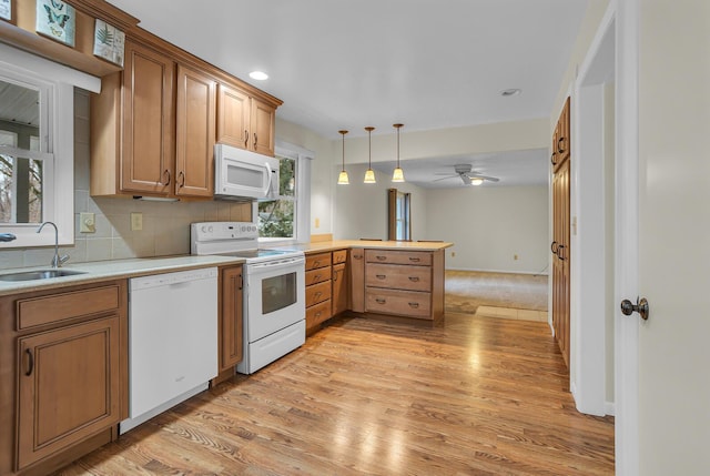 kitchen with light wood-style flooring, a peninsula, white appliances, a sink, and decorative backsplash