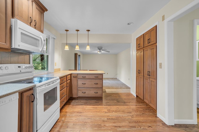 kitchen with light countertops, hanging light fixtures, light wood-style flooring, white appliances, and a peninsula