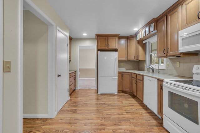 kitchen with white appliances, tasteful backsplash, light countertops, light wood-style floors, and a sink