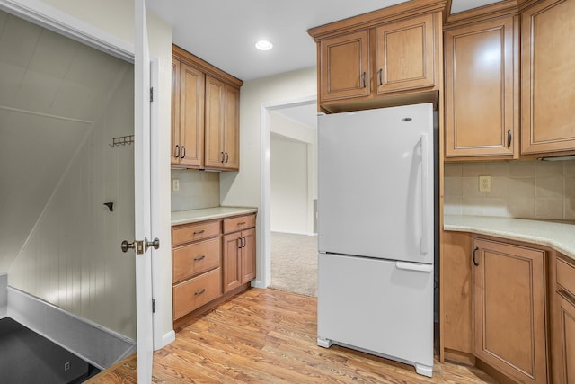 kitchen featuring light wood-style floors, backsplash, freestanding refrigerator, and brown cabinets