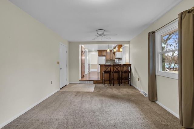 unfurnished living room featuring a ceiling fan, light colored carpet, visible vents, and baseboards